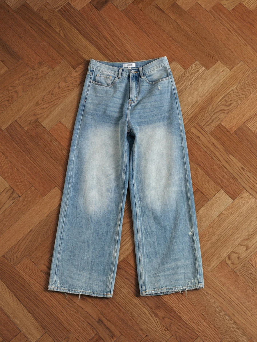 Original phone photo of the same jeans on a parquet floor